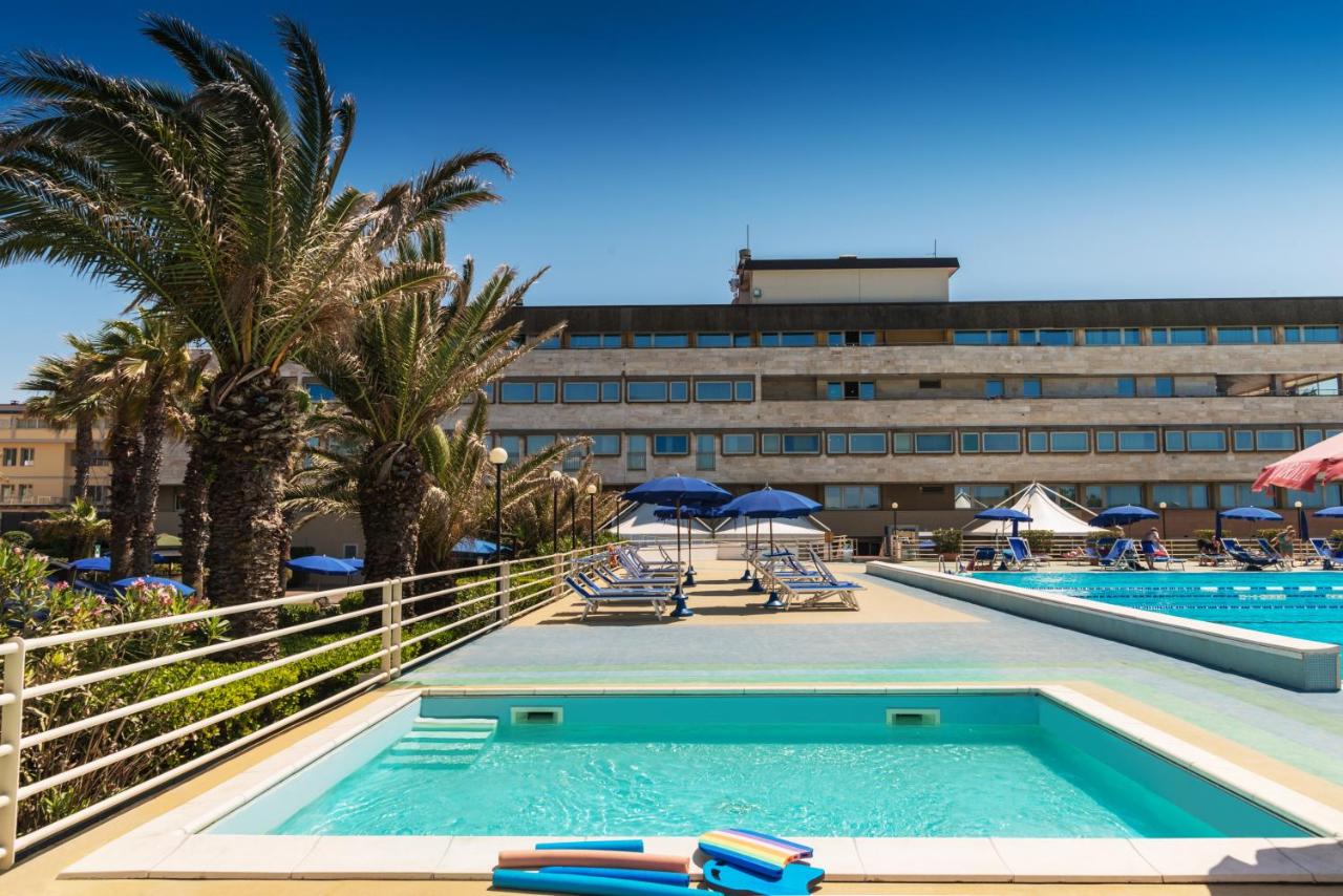 een zwembad bij een hotel met palmbomen en een gebouw bij Grand Hotel Continental in Tirrenia