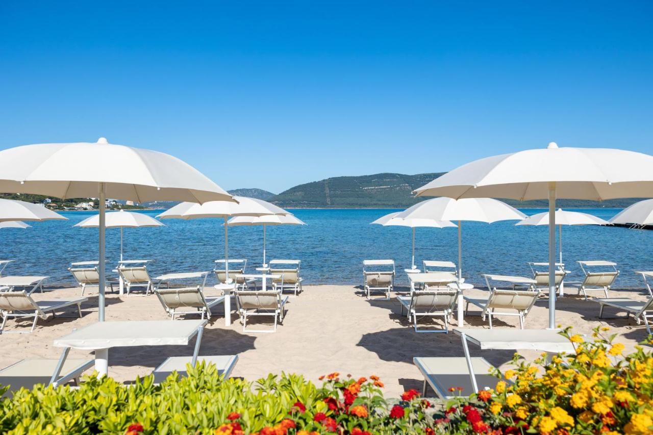 een groep stoelen en parasols op een strand bij Hotel Corte Rosada - Adults Only, Affiliated by Meliá in Porto Conte