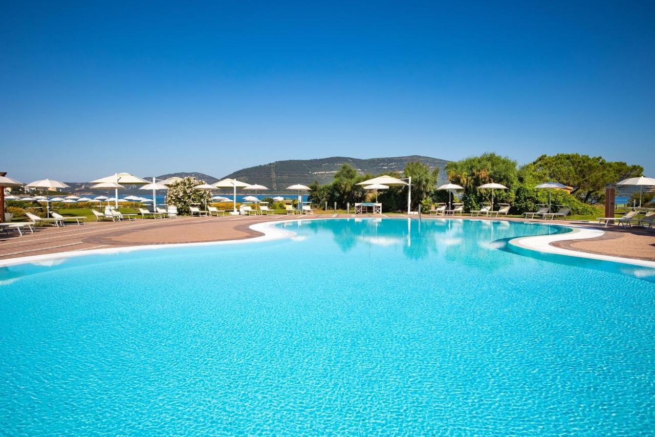 een groot zwembad met blauw water en parasols bij Hotel Corte Rosada - Adults Only, Affiliated by Meliá in Porto Conte