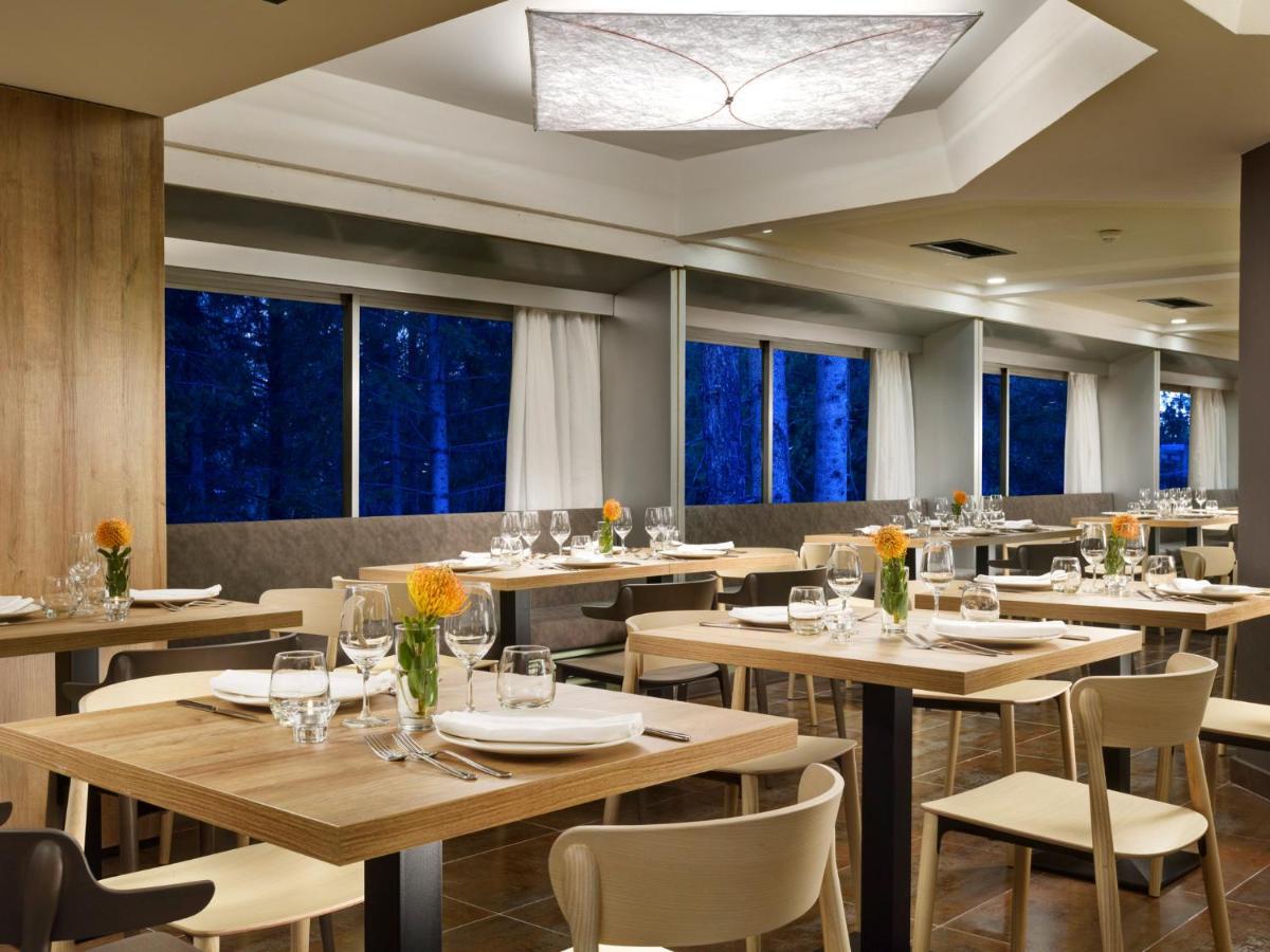 een restaurant met houten tafels en stoelen en ramen bij TH Marilleva in Mezzana