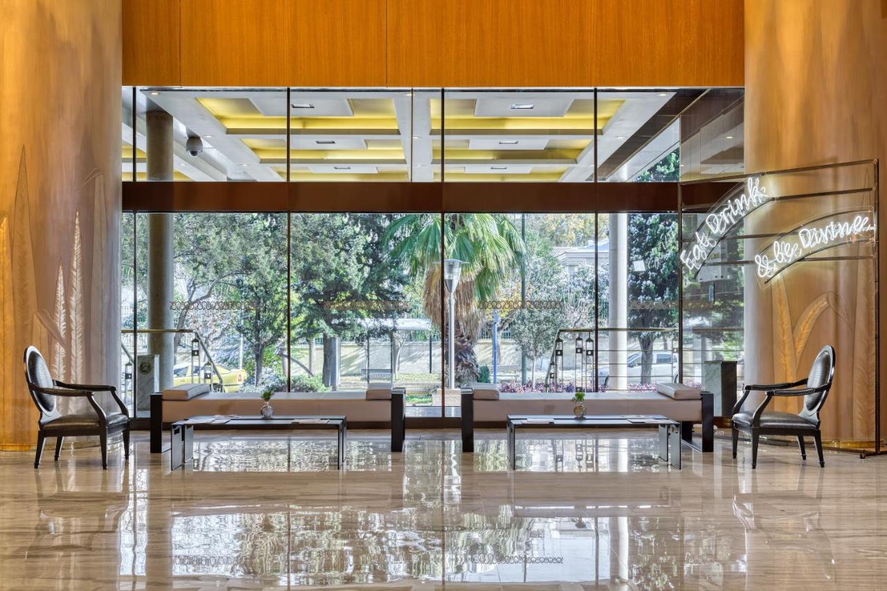 een lobby met tafels en stoelen en een groot raam bij Divani Caravel in Athene