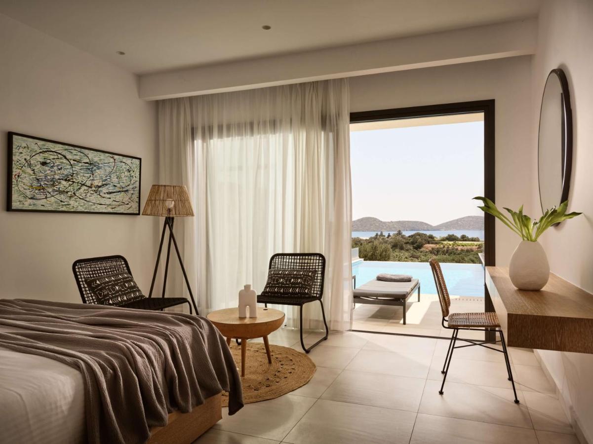 een slaapkamer met een bed, een tafel en stoelen bij Elounda Palm Hotel & Suites in Elounda