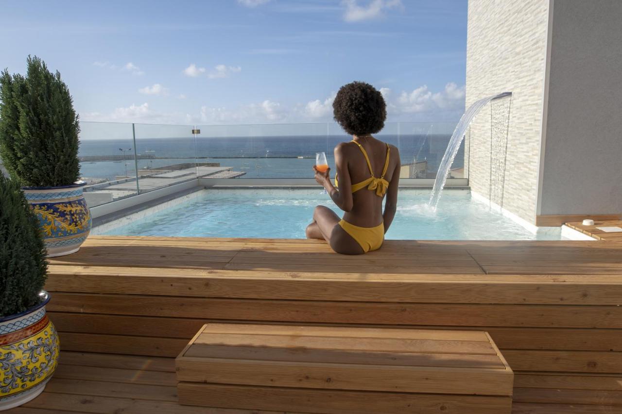 Een vrouw in een gele bikini zit naast een zwembad. bij Luxmarì Hotel & Spa in Castellammare del Golfo