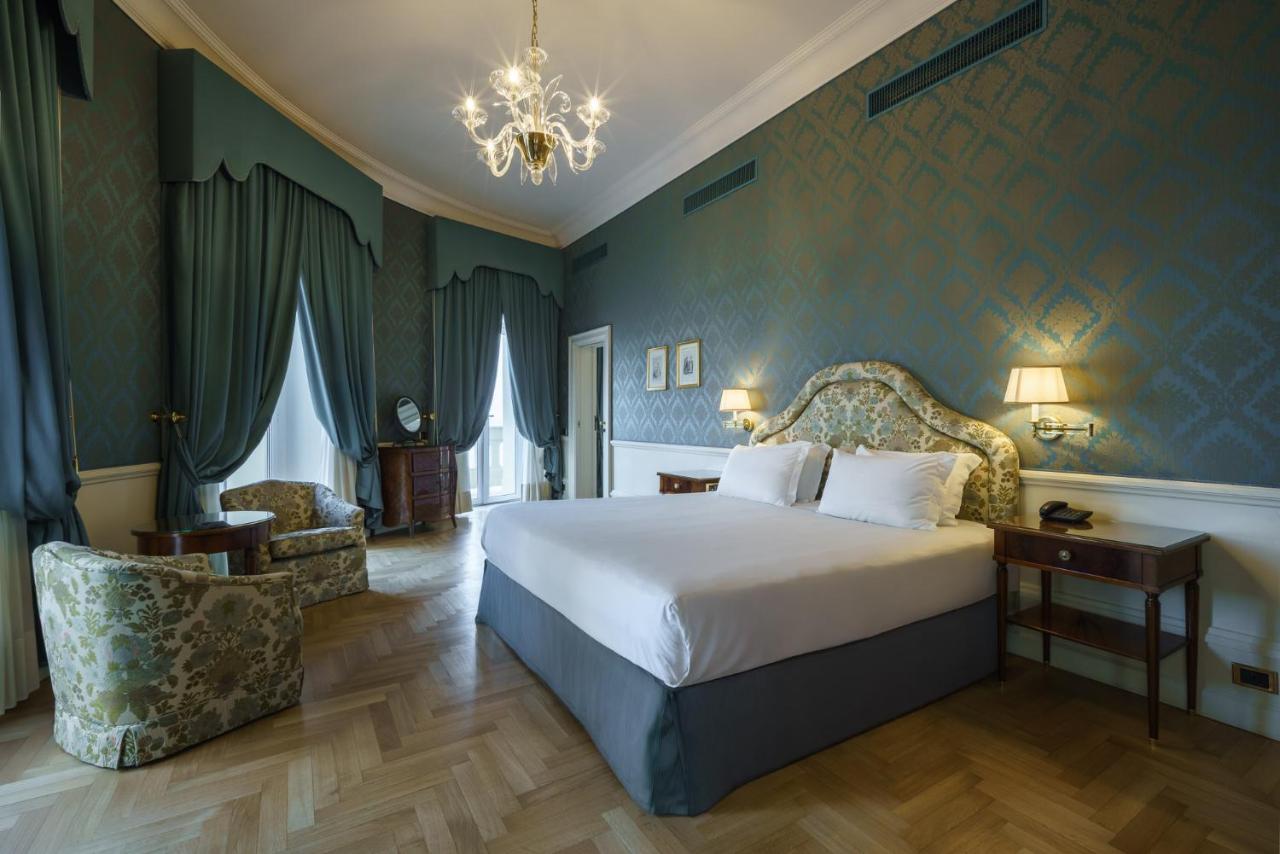 een slaapkamer met een groot bed en een kroonluchter bij Eurostars Hotel Excelsior in Napels