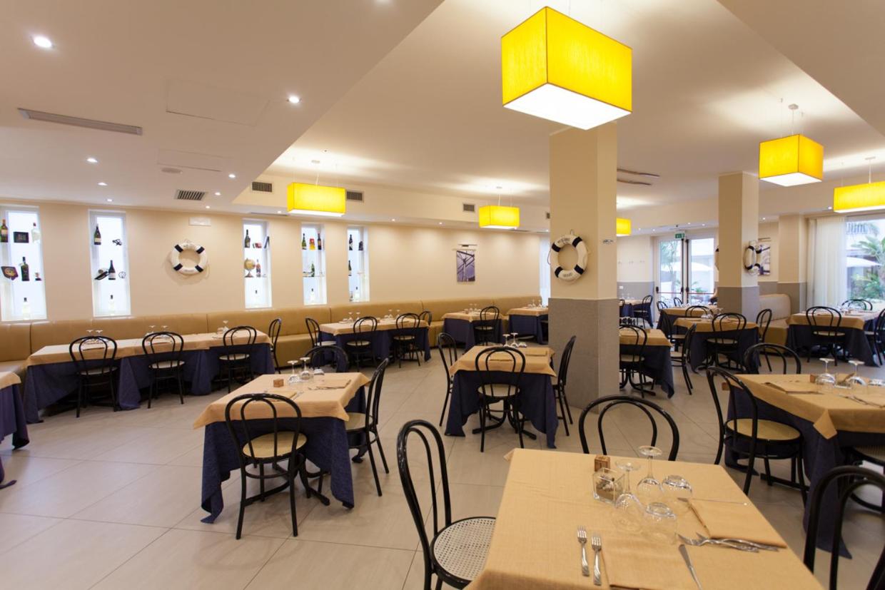 een eetkamer met tafels en stoelen en gele lampen bij Hotel Costazzurra Museum & Spa in San Leone