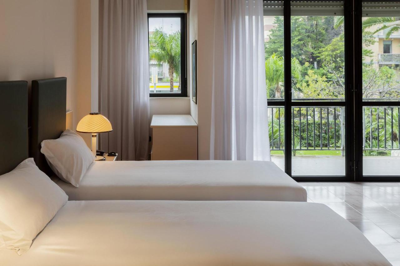 Twee bedden in een hotelkamer met een groot raam. bij B&B HOTEL Bari Rondò in Bari