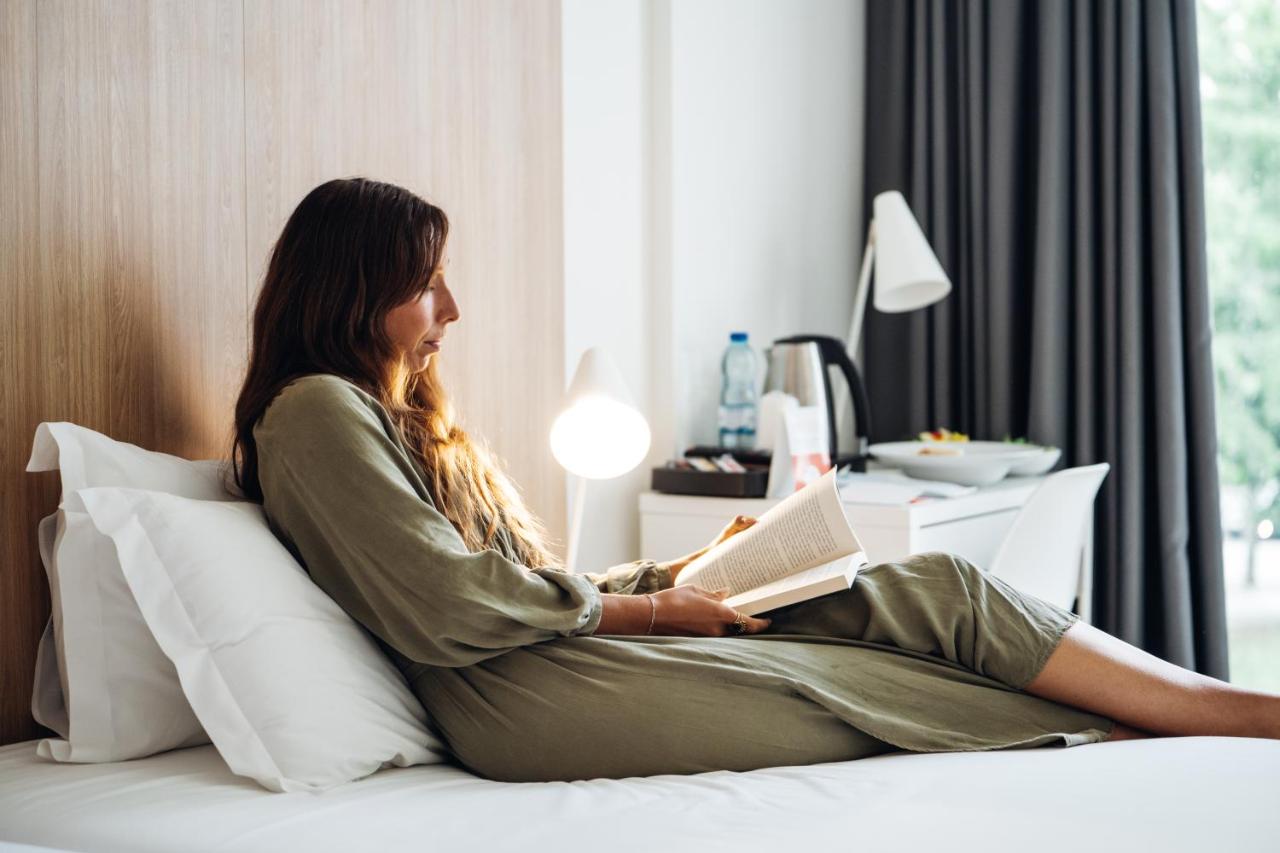 een vrouw zit op een bed en leest een boek bij Stay Hotel Porto Aeroporto in Maia