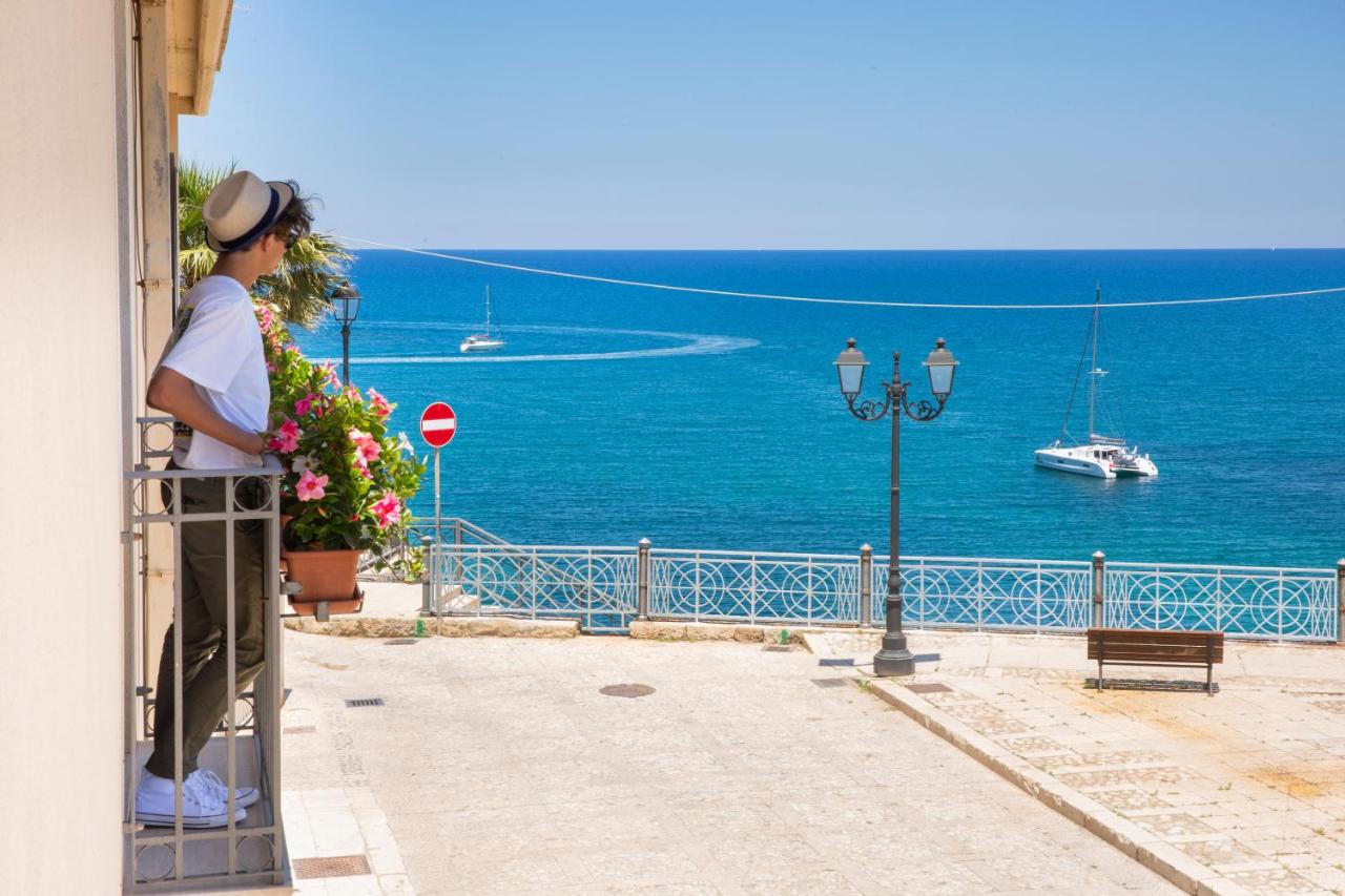 een man staat op een balkon en kijkt uit over de oceaan bij Hotel Al Madarig in Castellammare del Golfo