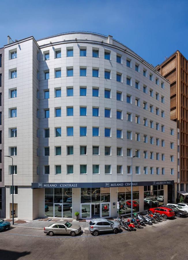 een groot wit gebouw met auto's geparkeerd op een parkeerplaats bij IH Hotels Milano Centrale in Milaan