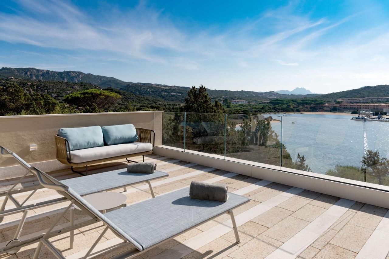 een balkon met een bank en uitzicht op het water bij 7Pines Resort Sardinia - A Destination By Hyatt in Baja Sardinia