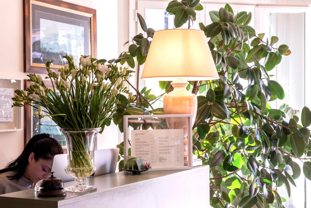 een vrouw die aan een bureau zit met een vaas bloemen bij Hotel Franceschi in Forte dei Marmi