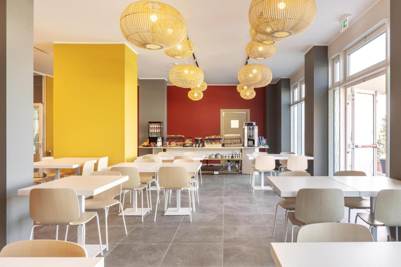 een restaurant met witte tafels en stoelen en kroonluchters bij B&B Hotel Roma Fiumicino Aeroporto Fiera 2 in Fiumicino