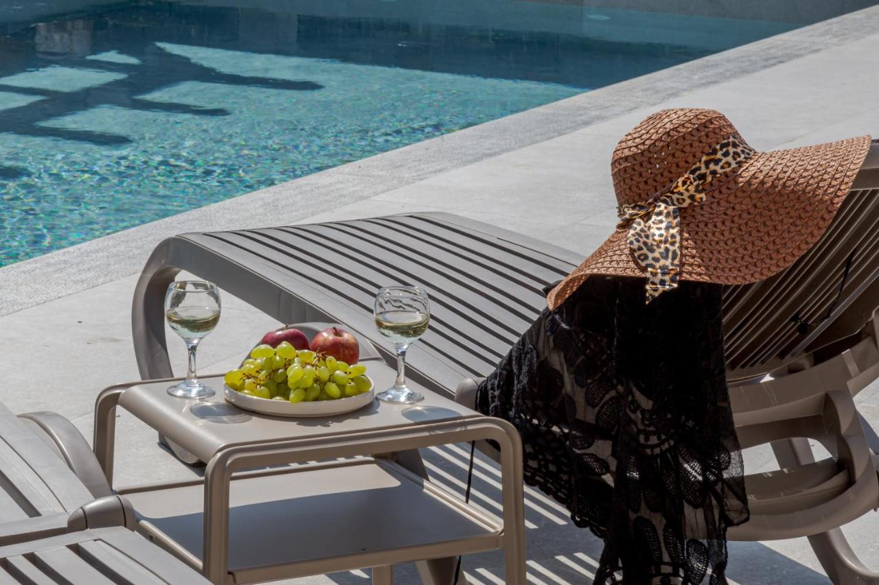 Een vrouw zit op een stoel met een fruitschaal en wijnglazen. bij Casa D'Oro Suites by Estia 'Adults Only' in Panormos R