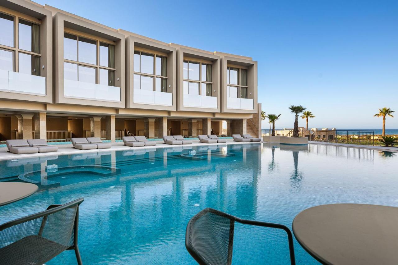 een zwembad met tafels en stoelen voor een gebouw bij Ventale Island Breeze Resort in Georgioupolis