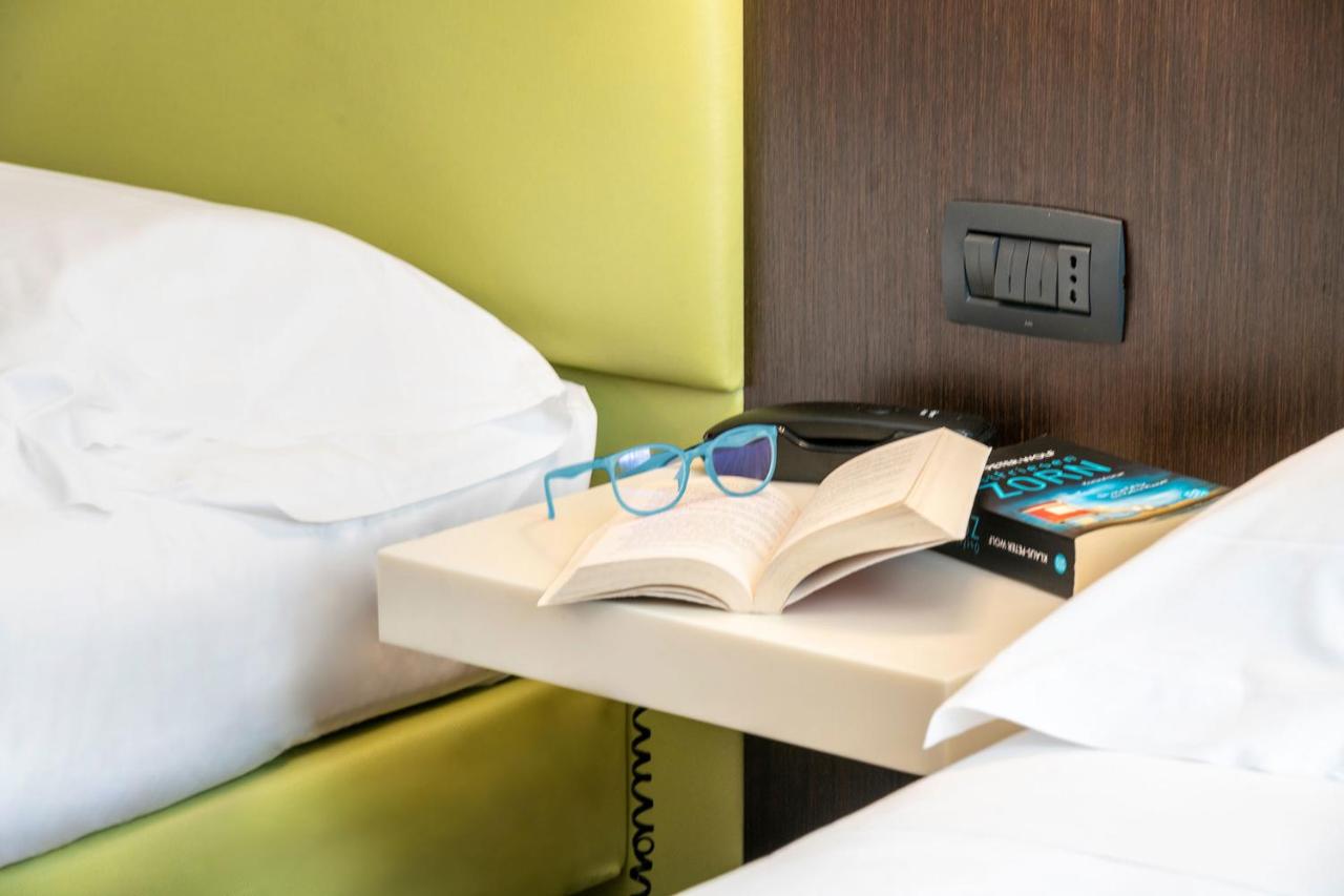 een tafel met een boek en een bril op een bed bij Kona Hotel Verona in Negrar