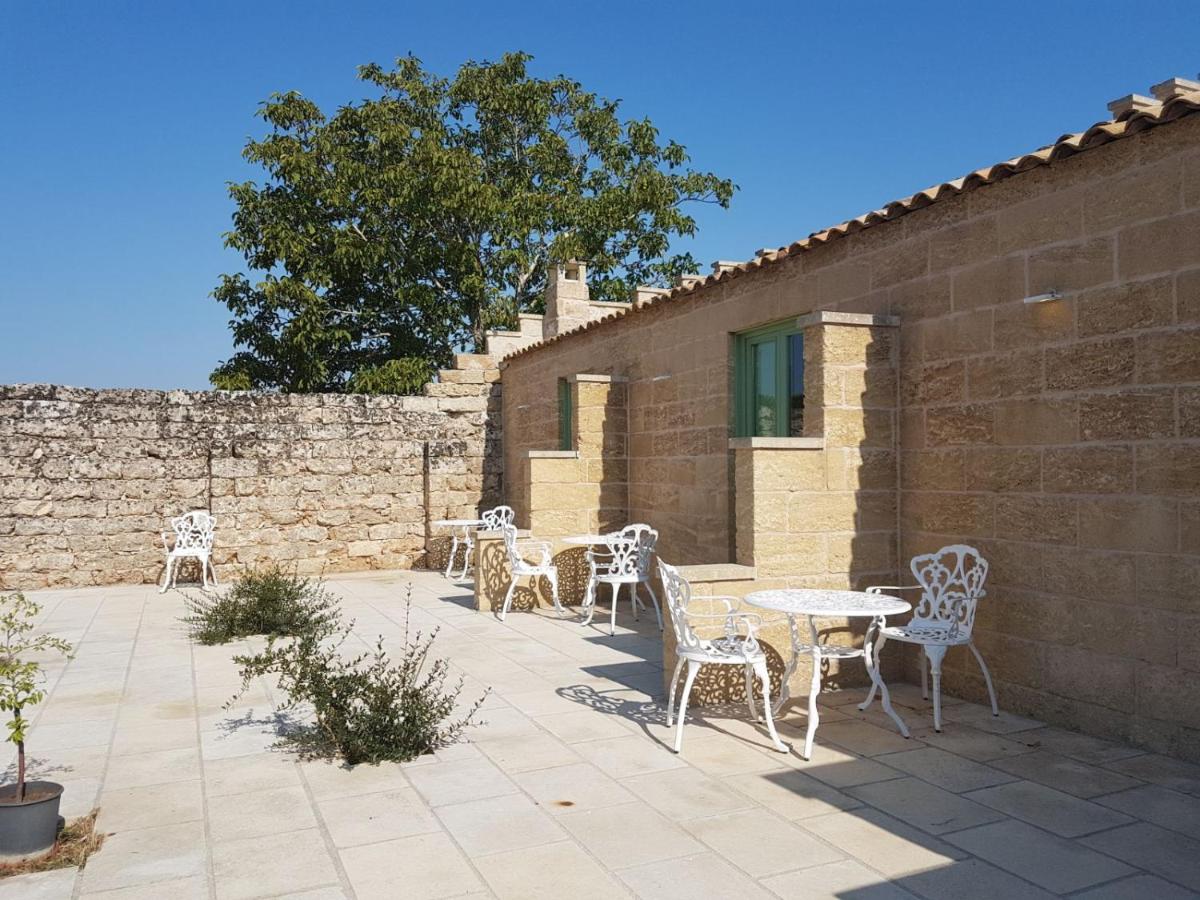 een terras met tafels en stoelen naast een bakstenen muur bij Masseria Costa in Corigliano dʼOtranto