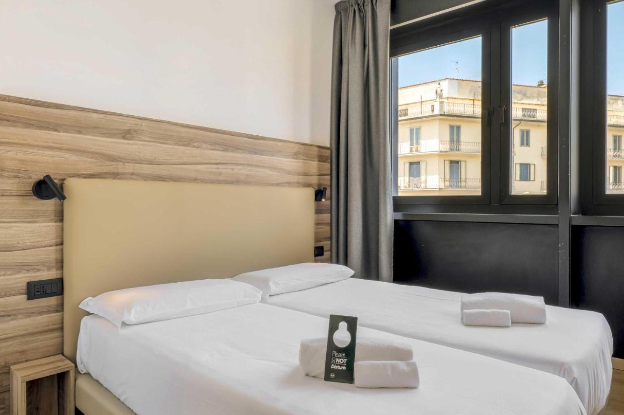 Twee bedden in een hotelkamer met een raam. bij B&B HOTEL Prato City Center in Prato