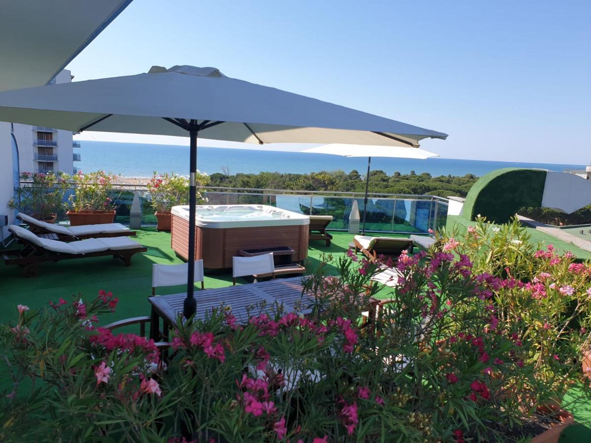 een terras met een parasol, stoelen en bloemen bij Hotel Cristallo in Lignano Sabbiadoro