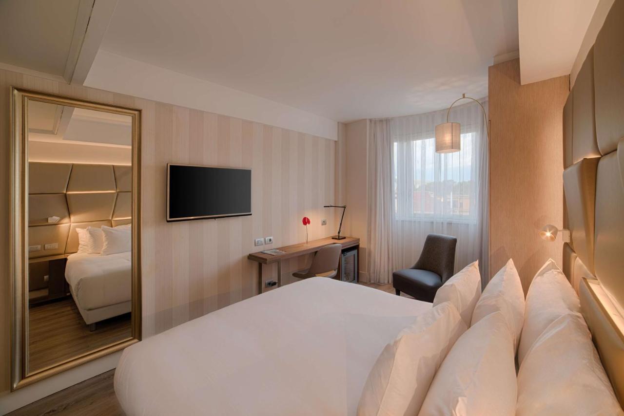 een hotelkamer met een wit bed en een spiegel bij NH Collection Roma Centro in Rome