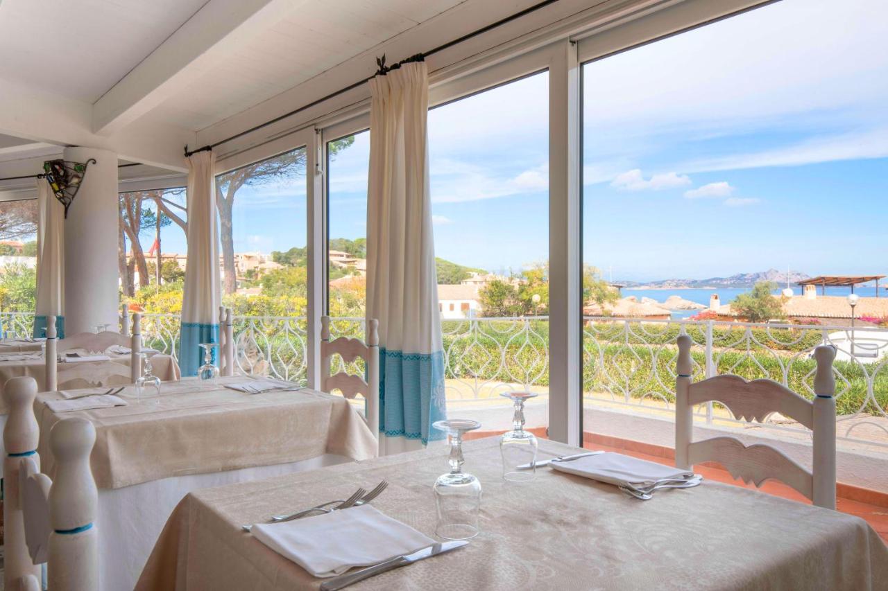 een eetkamer met twee tafels en een groot raam bij HOTIDAY Room Collection - Baja Sardinia in Baja Sardinia