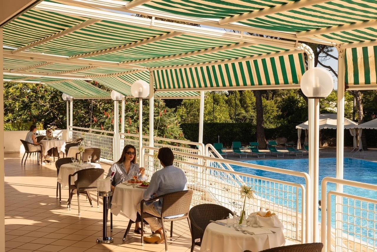 Twee mensen zitten aan tafels op een terras bij een zwembad. bij Hotel Sierra Silvana in Selva di Fasano