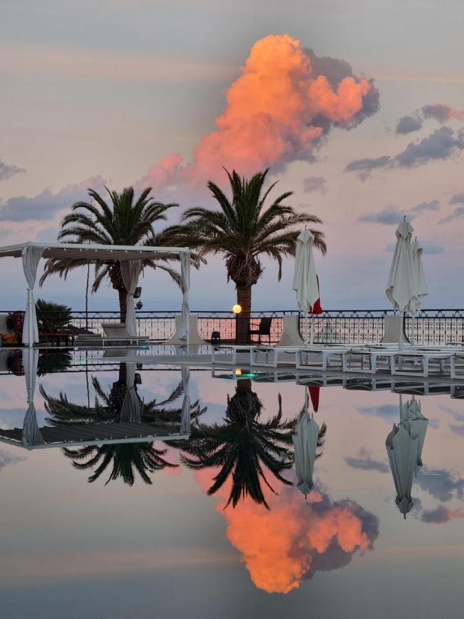 een weerspiegeling van een zwembad met palmbomen en parasols bij Delta Hotels by Marriott Giardini Naxos in Giardini Nax