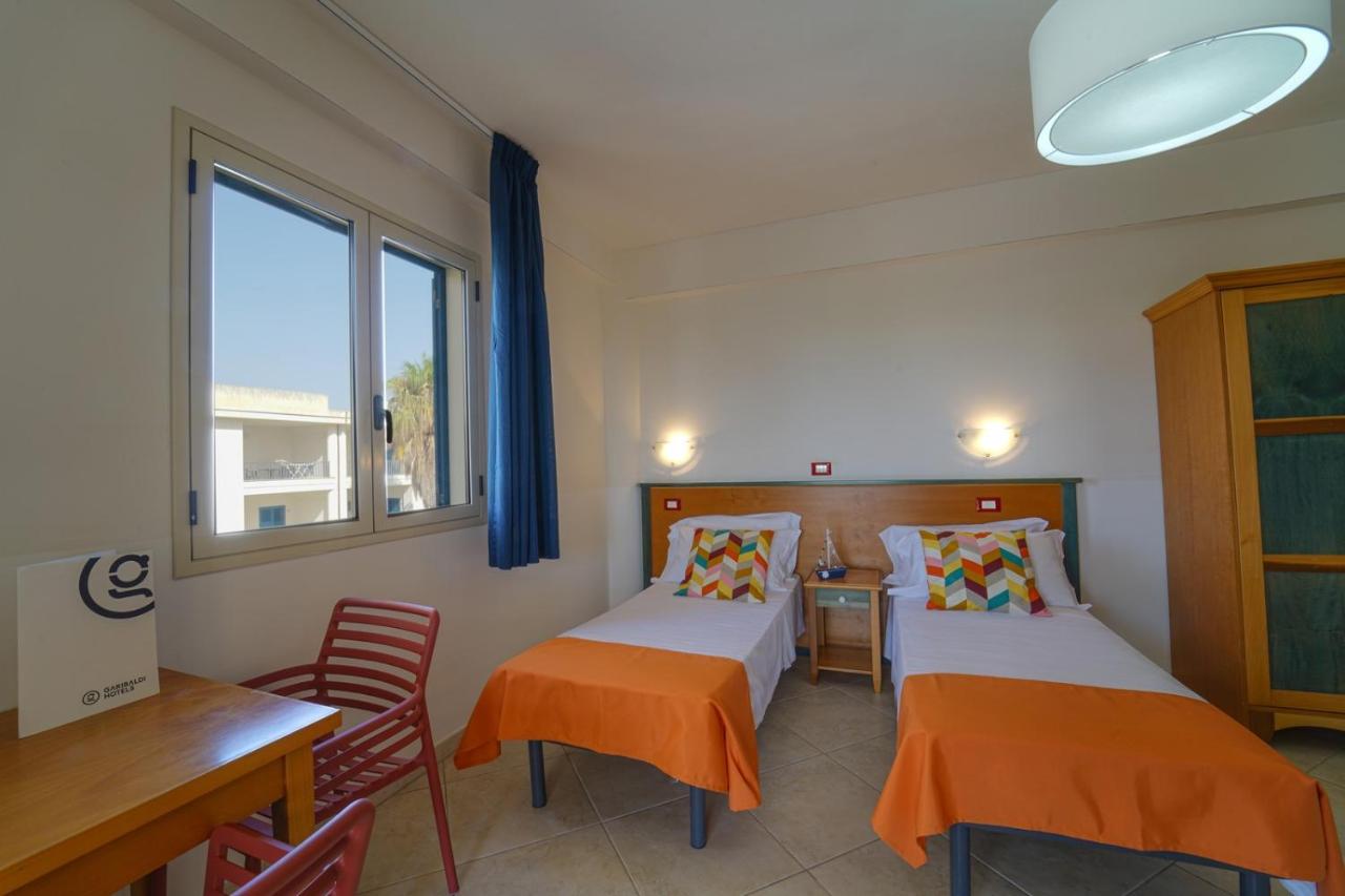 een kamer met twee bedden, een tafel en een raam bij GH Baraka Village in Scoglitti