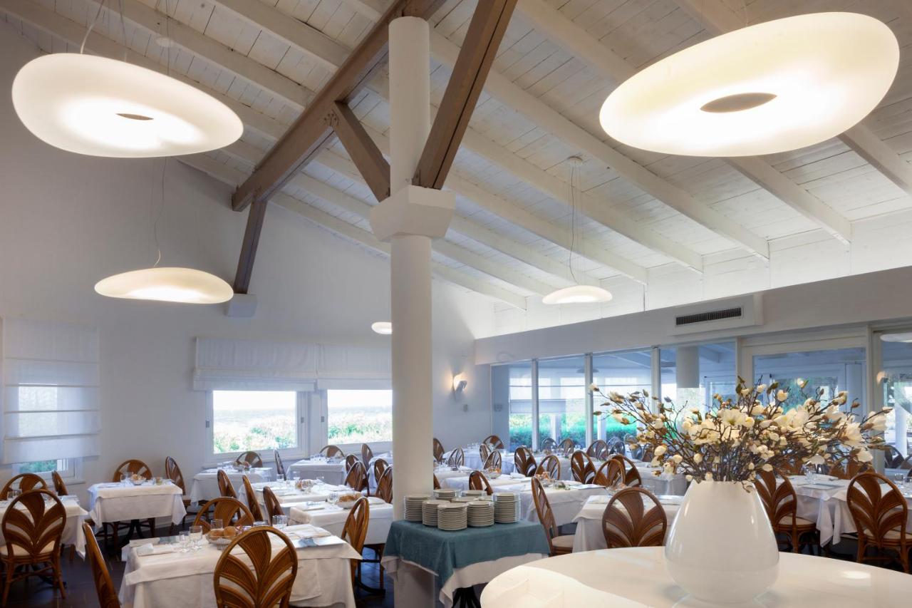 een restaurant met witte tafels en stoelen en een vaas met bloemen bij Hotel Mare Pineta in Santa Margherita di Pula