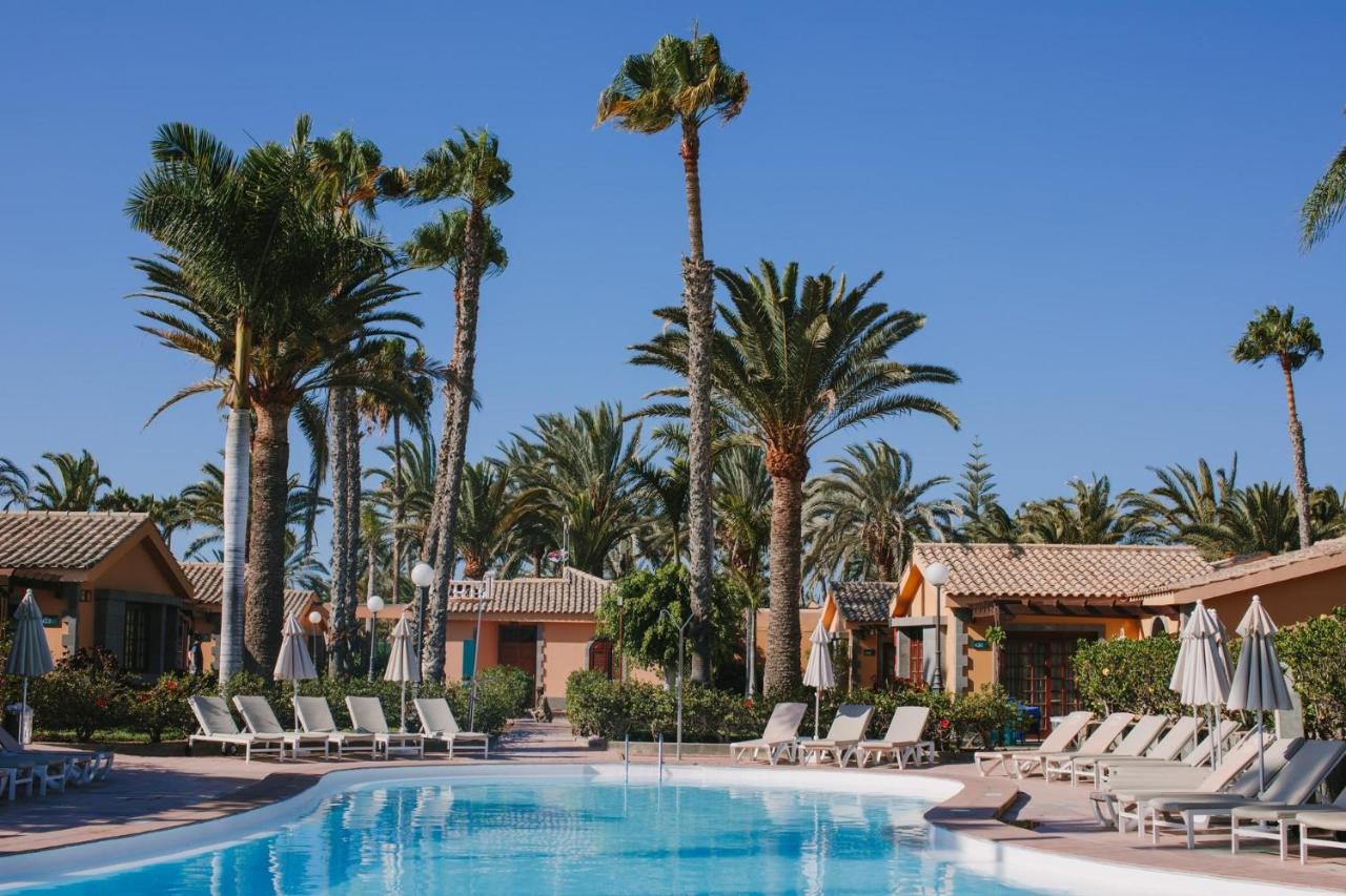 een zwembad bij het resort met ligstoelen en palmbomen bij Maspalomas Resort by Dunas in Maspalomas