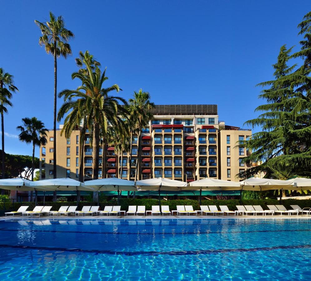 een zwembad met ligstoelen en een hotel op de achtergrond bij Parco dei Principi Grand Hotel & SPA Roma - Preferred Hote