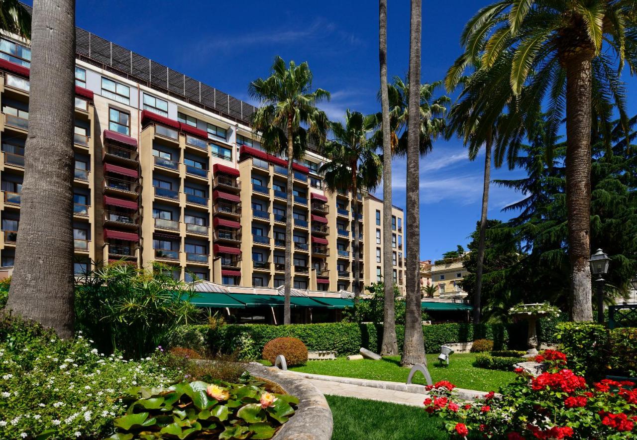 een gebouw met palmbomen en bloemen in een park bij Parco dei Principi Grand Hotel & SPA Roma - Preferred Hotels & Resor
