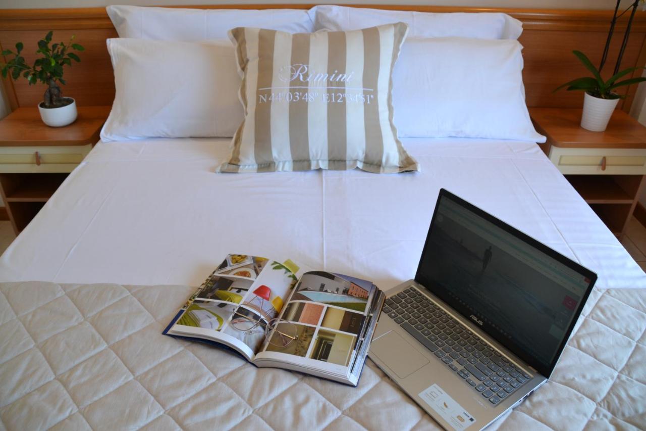een laptop op een bed met een tijdschrift en een boek bij Hotel Apogeo - Breakfast Experience in Rimini