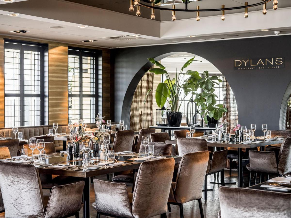 een restaurant met tafels en stoelen in een ruimte met ramen bij Alexander Hotel in Noordwijk aan Zee +65 foto's