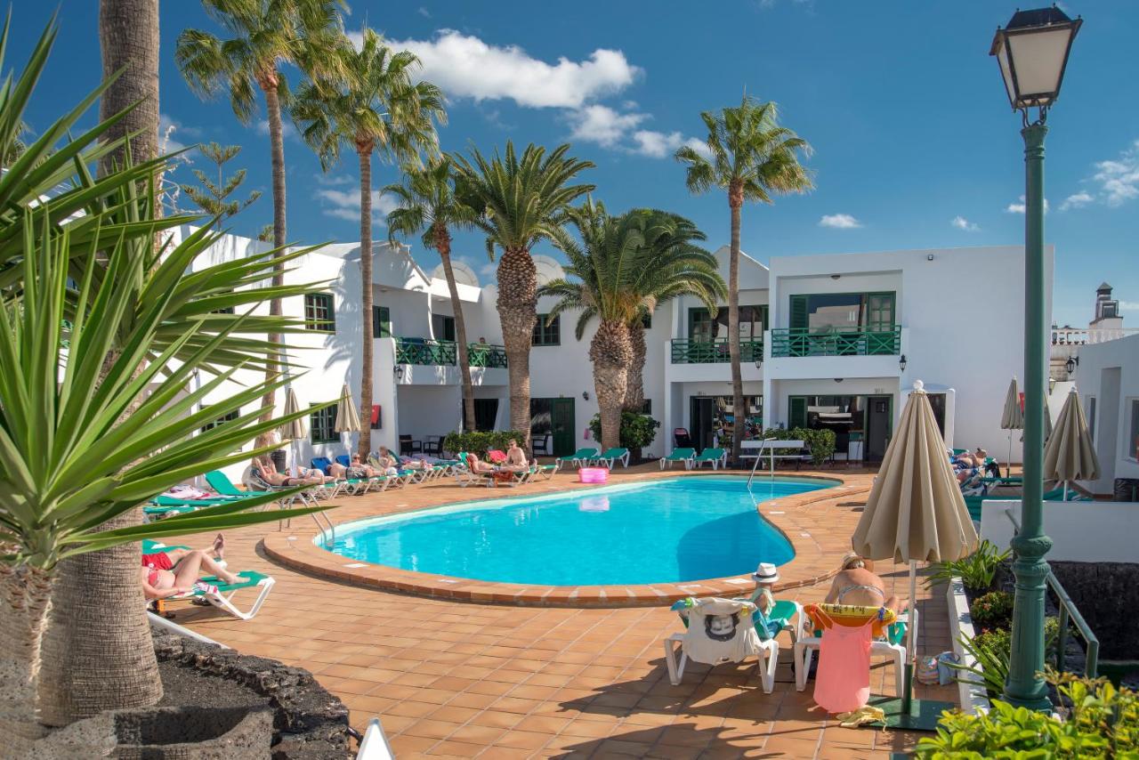 een zwembad met palmbomen en mensen die eromheen zitten bij Rocas Blancas Apartments in Puerto del Carmen