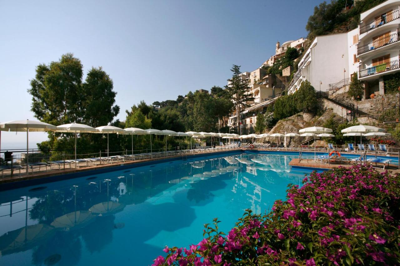 een zwembad met blauw water, parasols en bloemen bij Hotel Royal Positano in Positano
