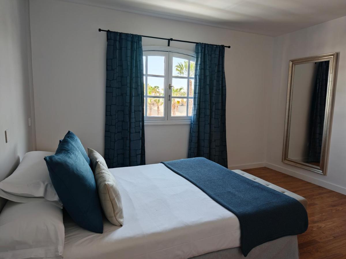 een slaapkamer met een bed met blauwe kussens en een raam bij Apartamentos San Marcial in Tías +16 foto's