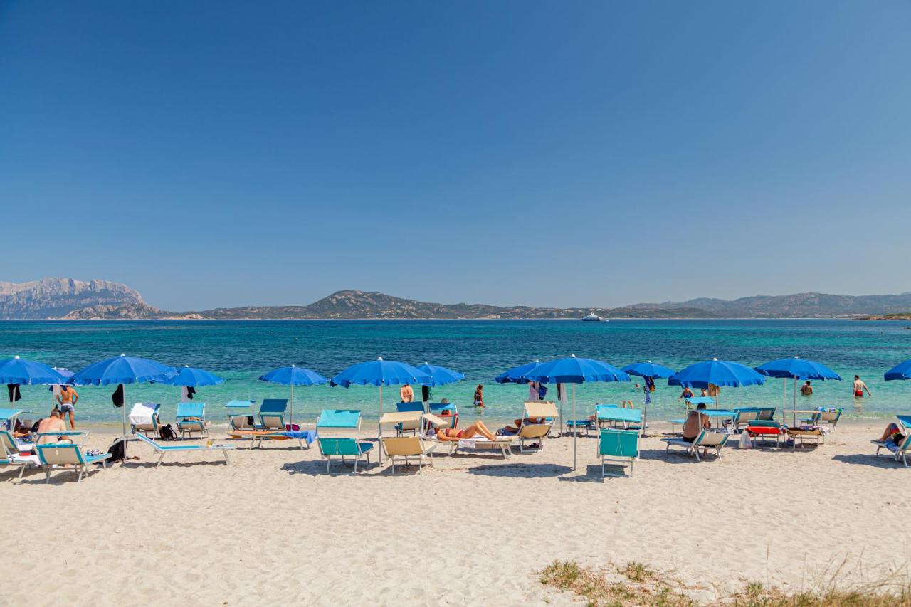 een groep mensen die op een strand zitten met blauwe parasols bij Hotel Mare Blue in Olbia