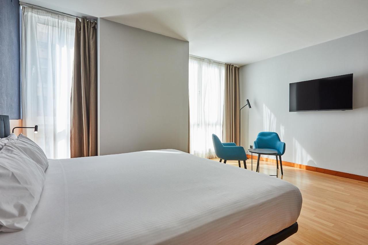 een slaapkamer met een bed, twee stoelen en een tv bij Silken Sant Gervasi in Barcelona