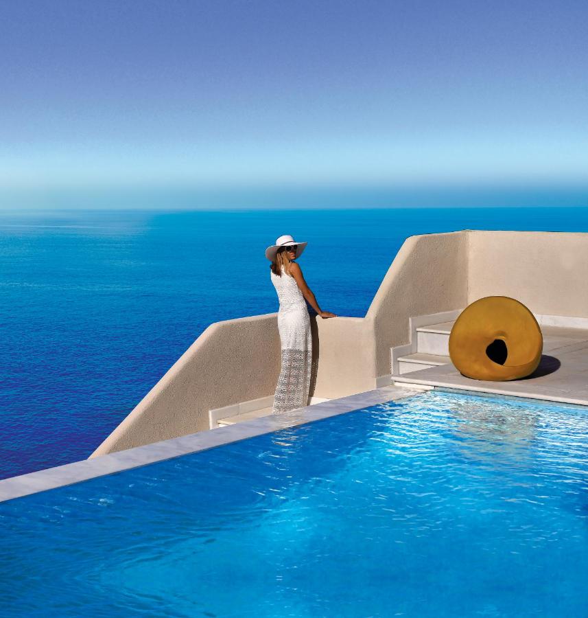Een vrouw in een witte jurk staat naast een zwembad. bij Out Of The Blue Resort & Spa in Agia Pelagia