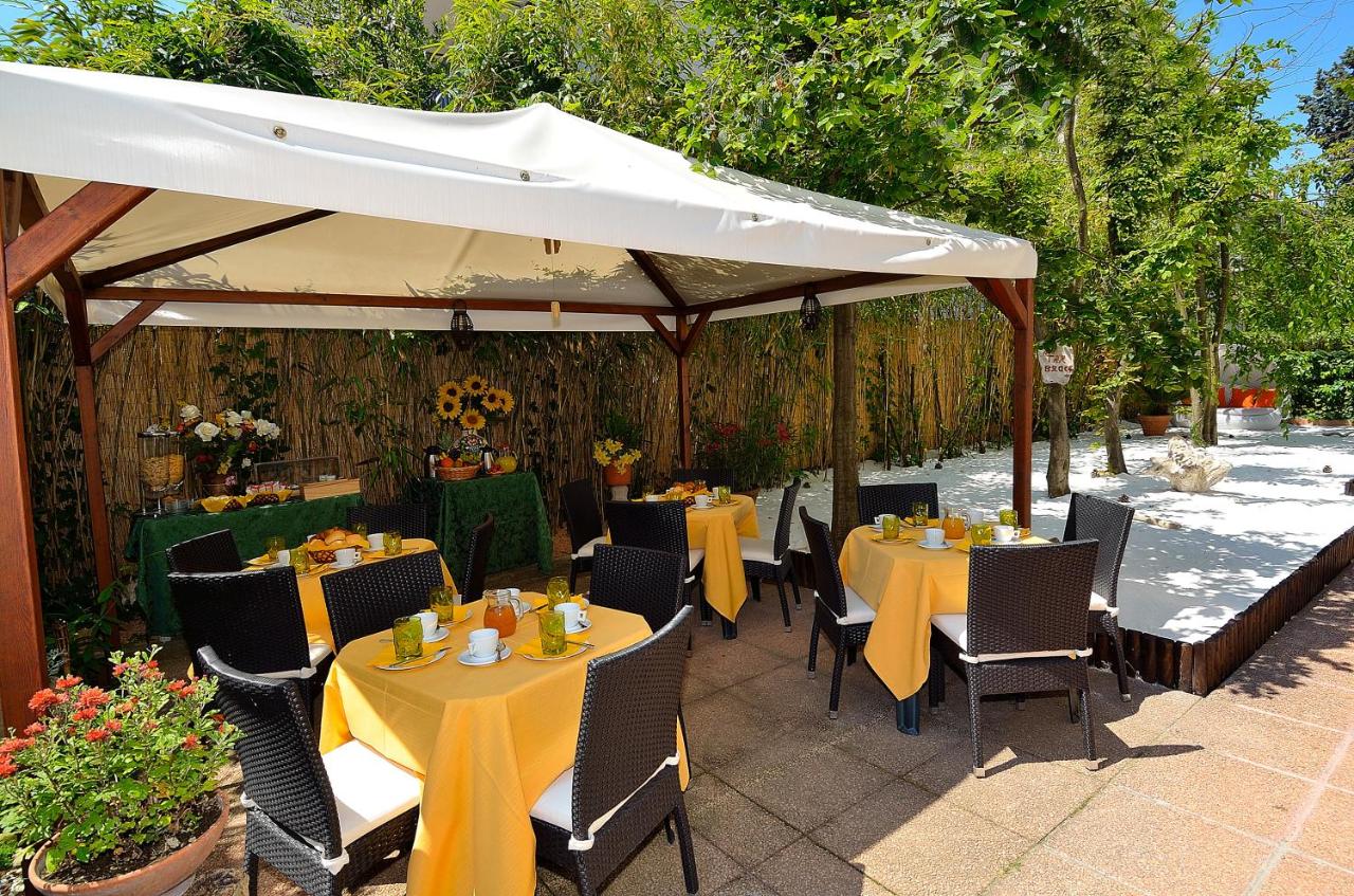 een terras met tafels en stoelen onder een witte parasol bij Villa Angelica in Venetië-Lido