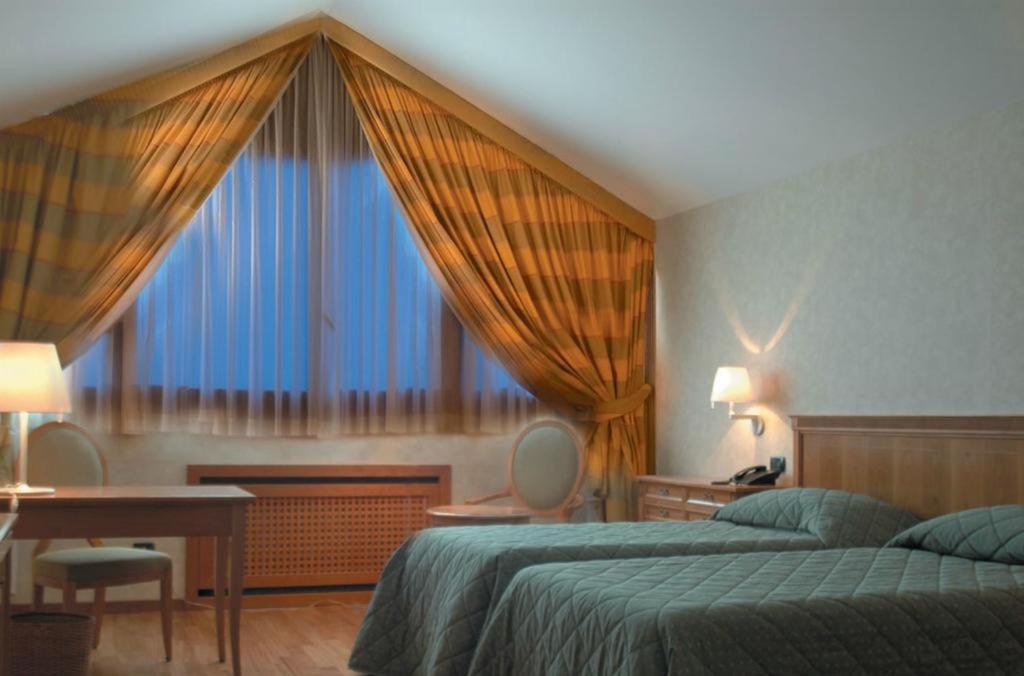een slaapkamer met twee bedden, een bureau en een raam bij Monica Hotel Fiera in Pregnana Milanese