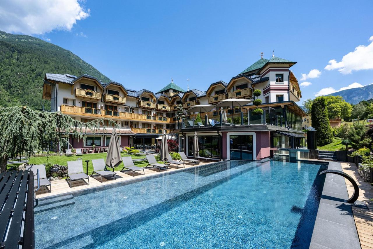 een hotel met een zwembad met ligstoelen en een gebouw bij Tevini Dolomites Charming Hotel in Commezzadura