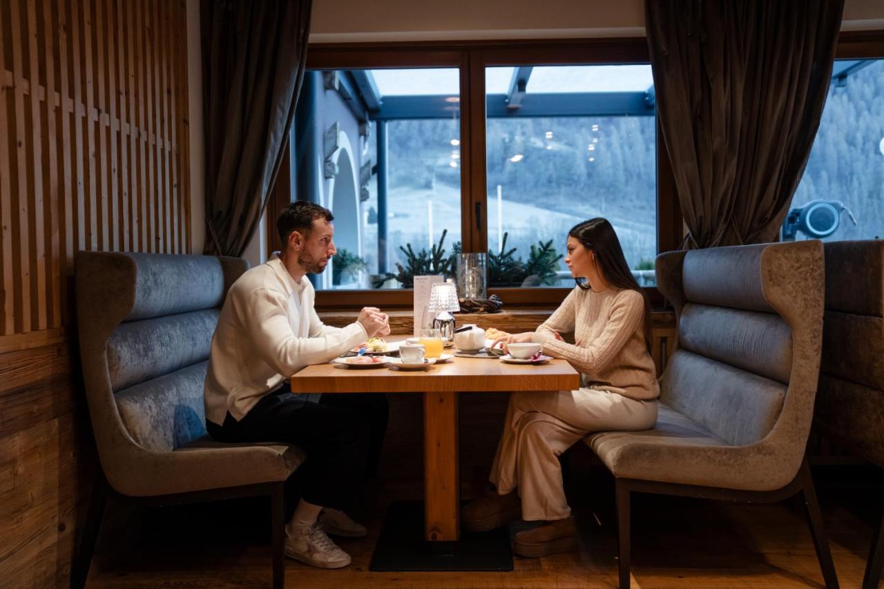een man en een vrouw zitten aan een tafel in een restaurant bij Tevini Dolomites Charming Hotel in Commezzadura