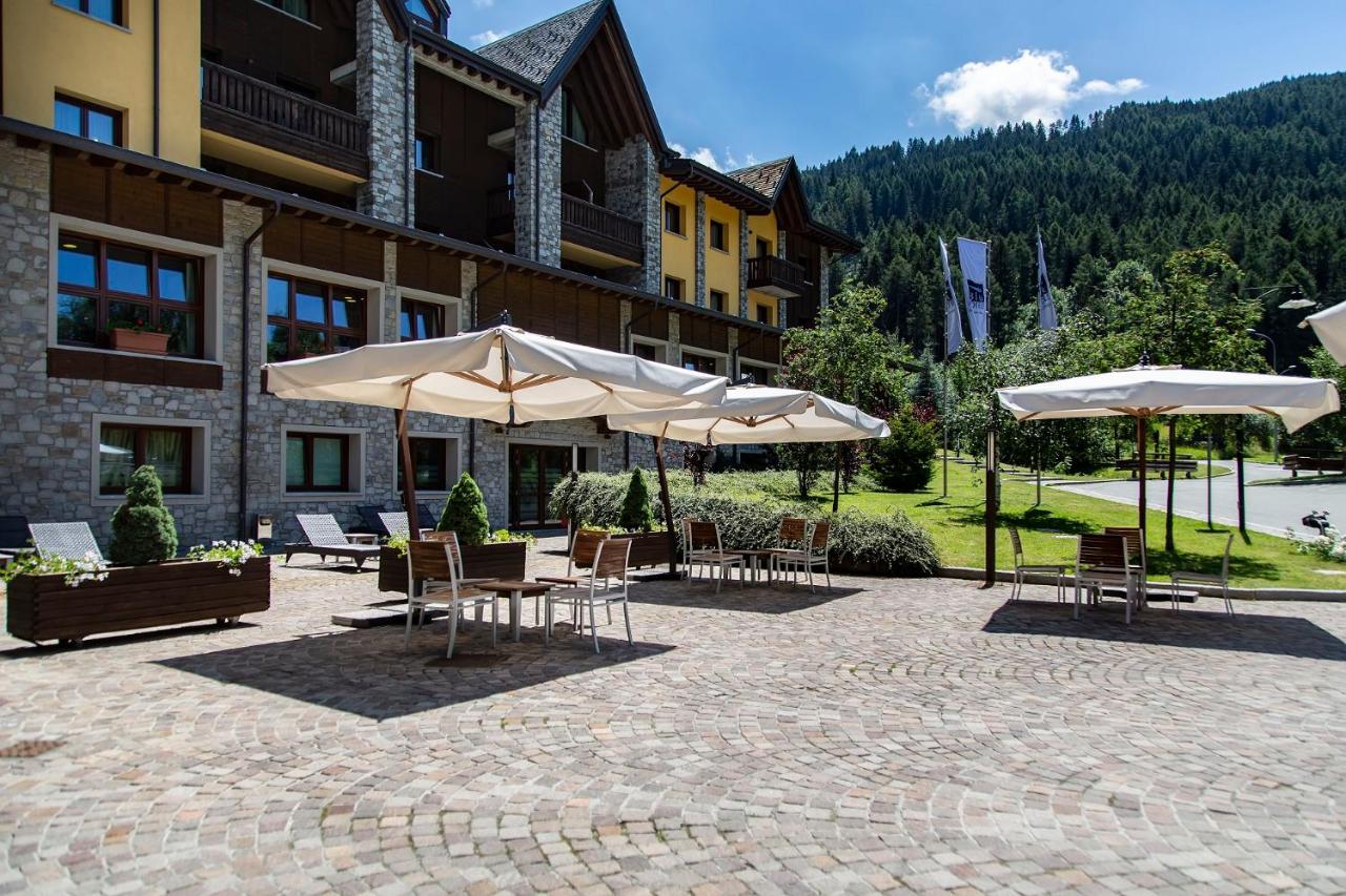 een terras met tafels en parasols voor een gebouw bij Blu Hotel Acquaseria in Ponte di Legno