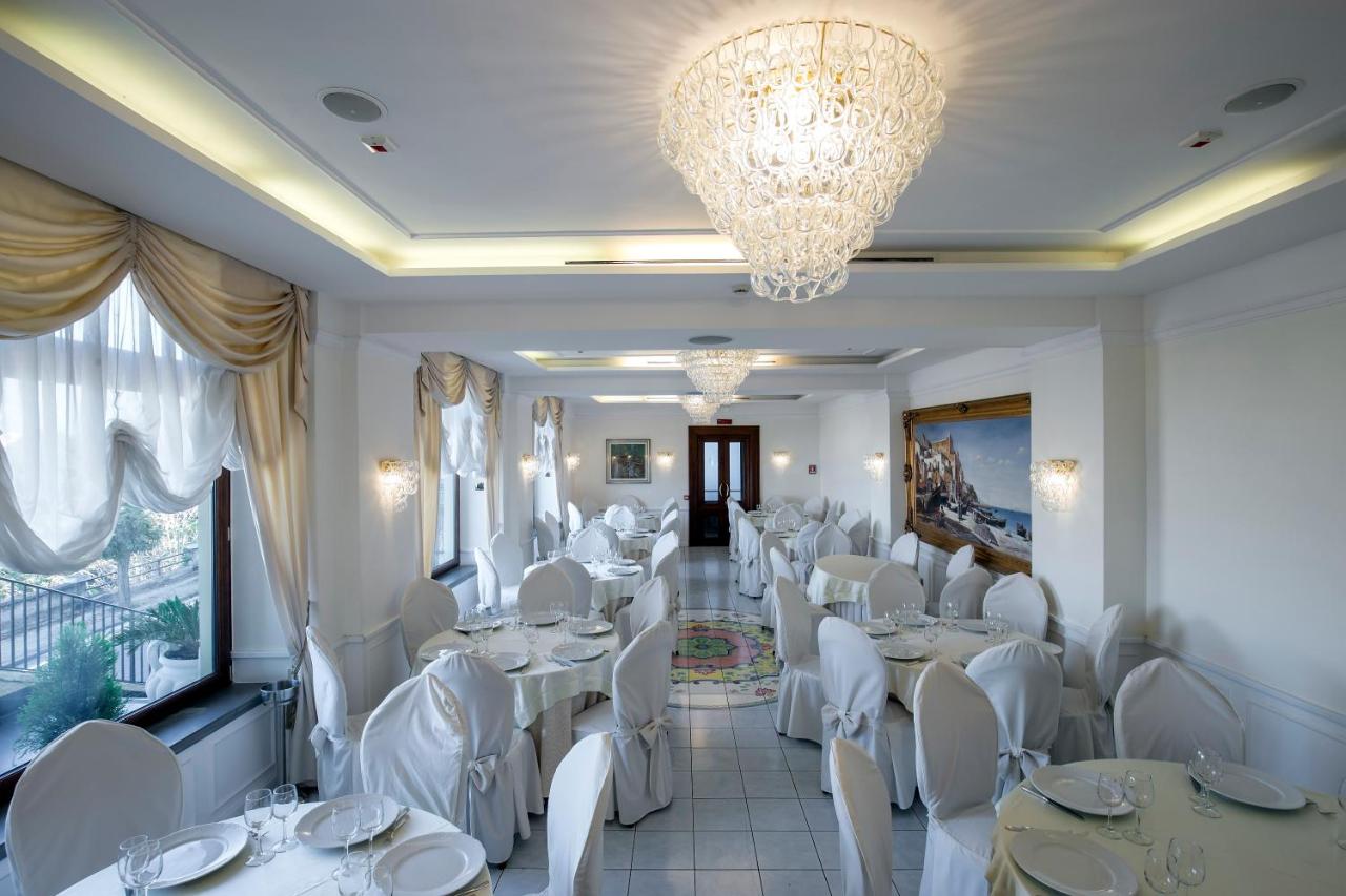 een restaurant met witte tafels en stoelen en een kroonluchter bij La Panoramica Hotel in Castellammare di Stabia