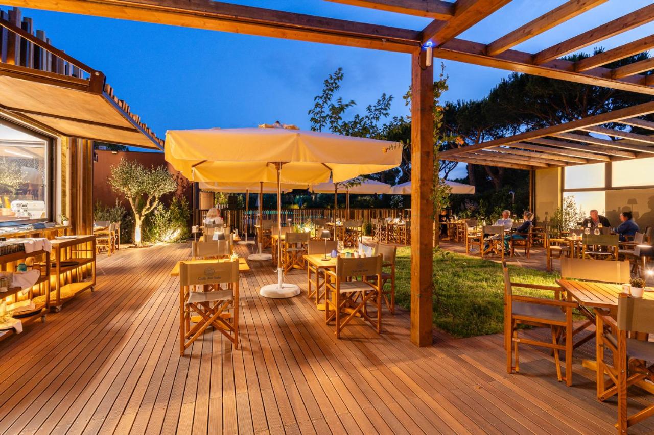 een houten terras met tafels en stoelen en een parasol bij Club del Sole Orbetello Family Collection in Orbetello