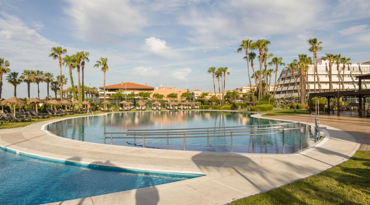 een zwembad bij een resort met palmbomen bij Ilunion Islantilla in Islantilla