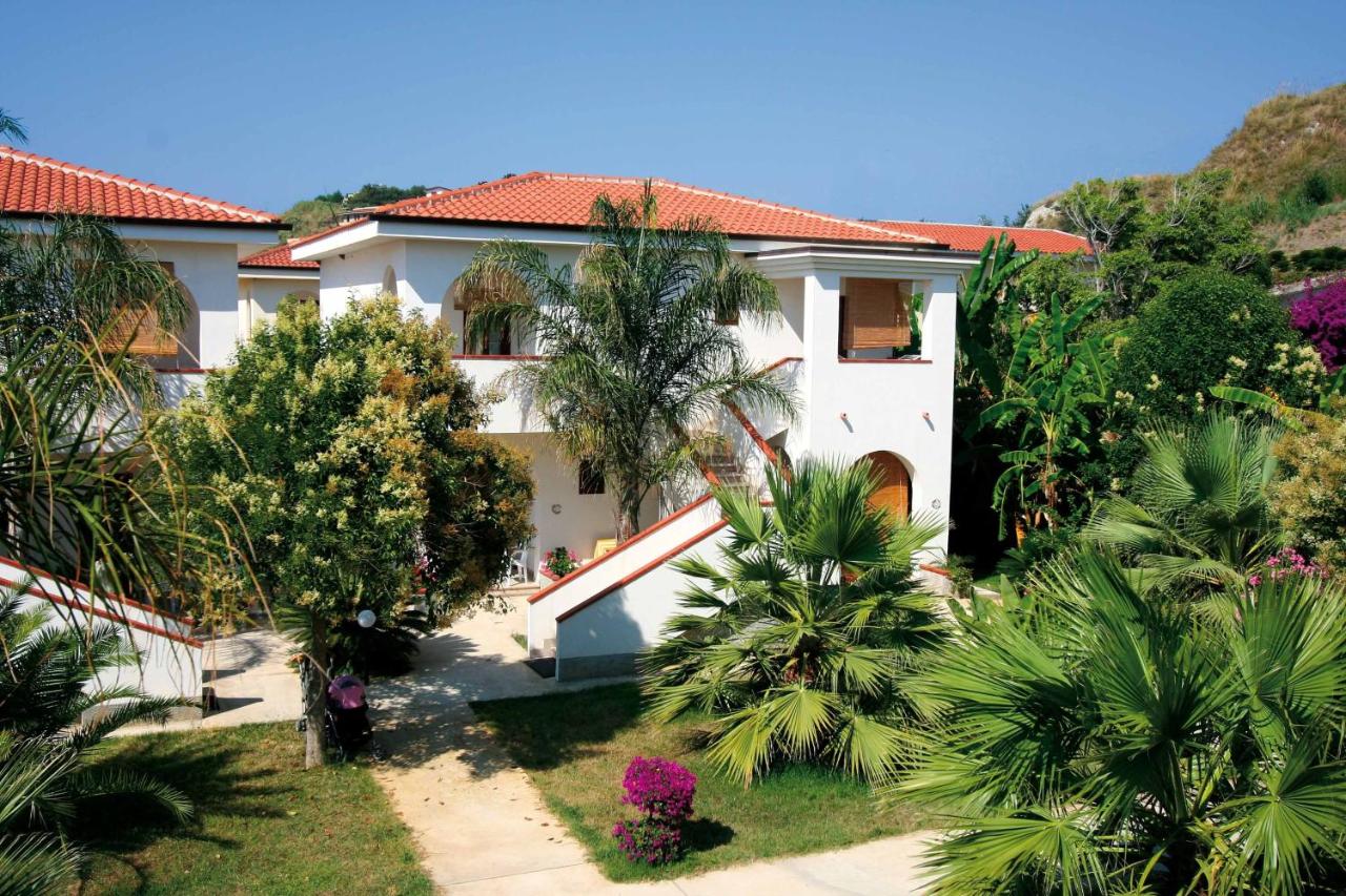 een wit huis met palmbomen ervoor bij Villaggio Torre Ruffa Robinson in Capo Vaticano