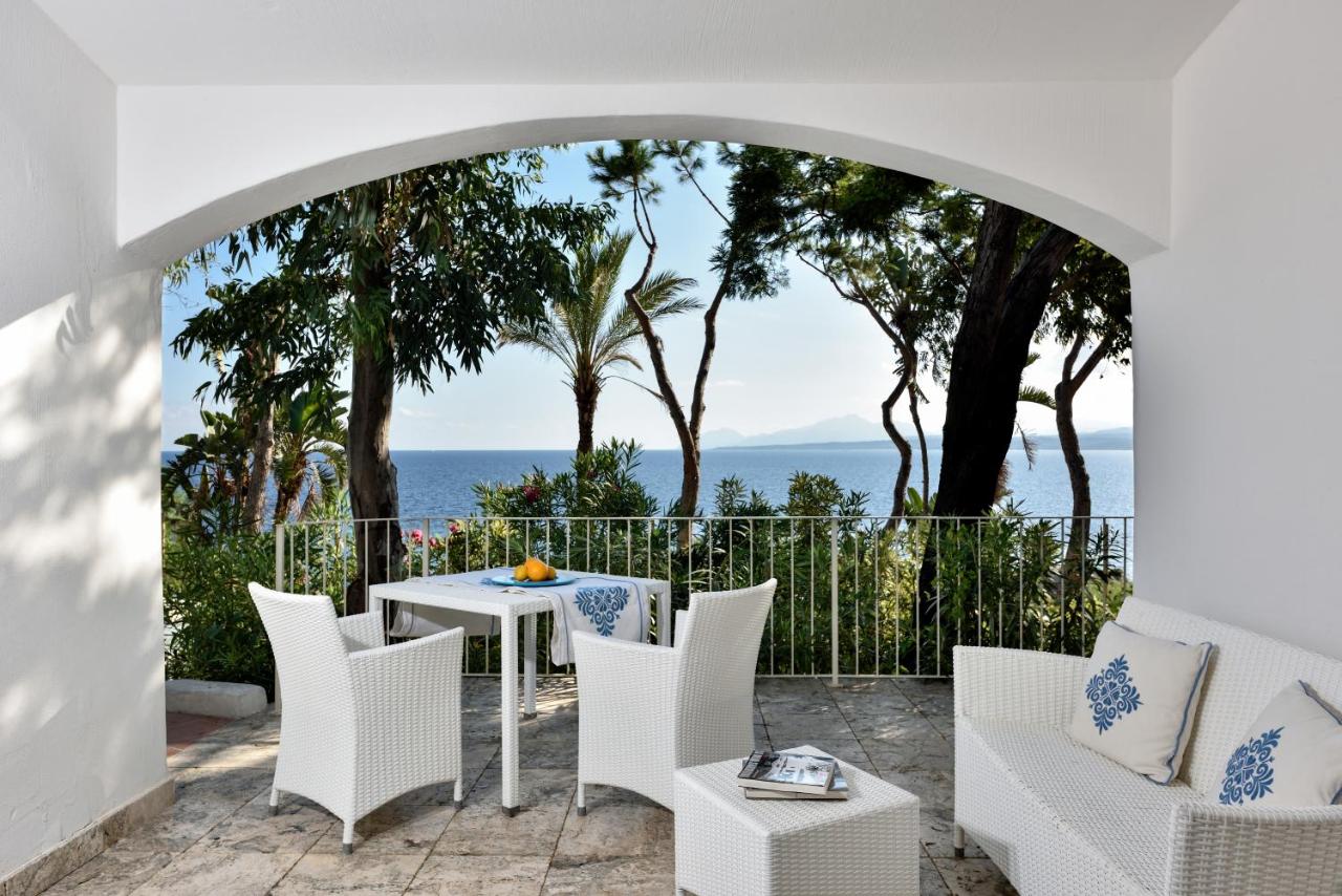 een terras met een tafel en stoelen en uitzicht op de oceaan bij Arbatax Park Resort - Cottage by Falkensteiner in Àrbat