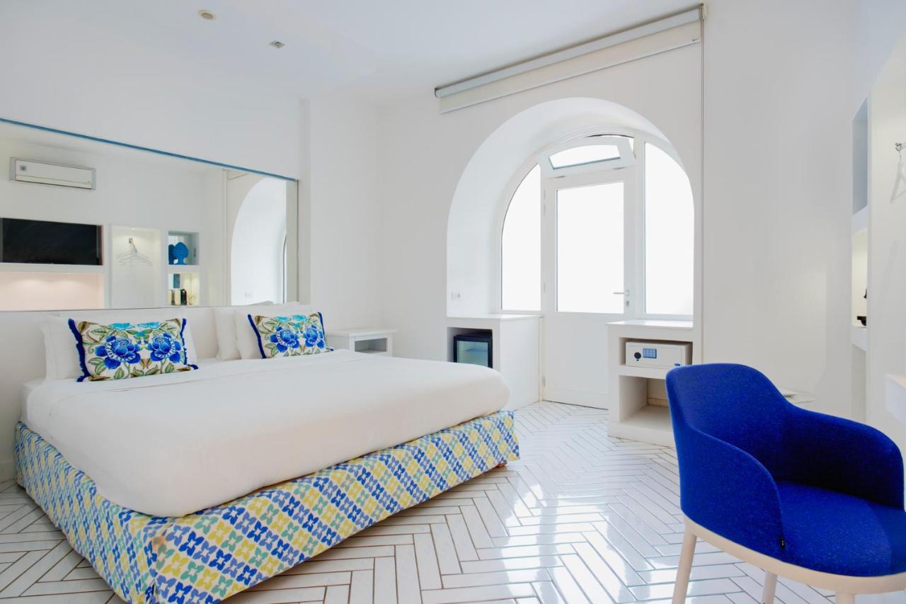een witte slaapkamer met een groot bed en een blauwe stoel bij Relais Correale Rooms & Garden in Sorrento +33 foto's